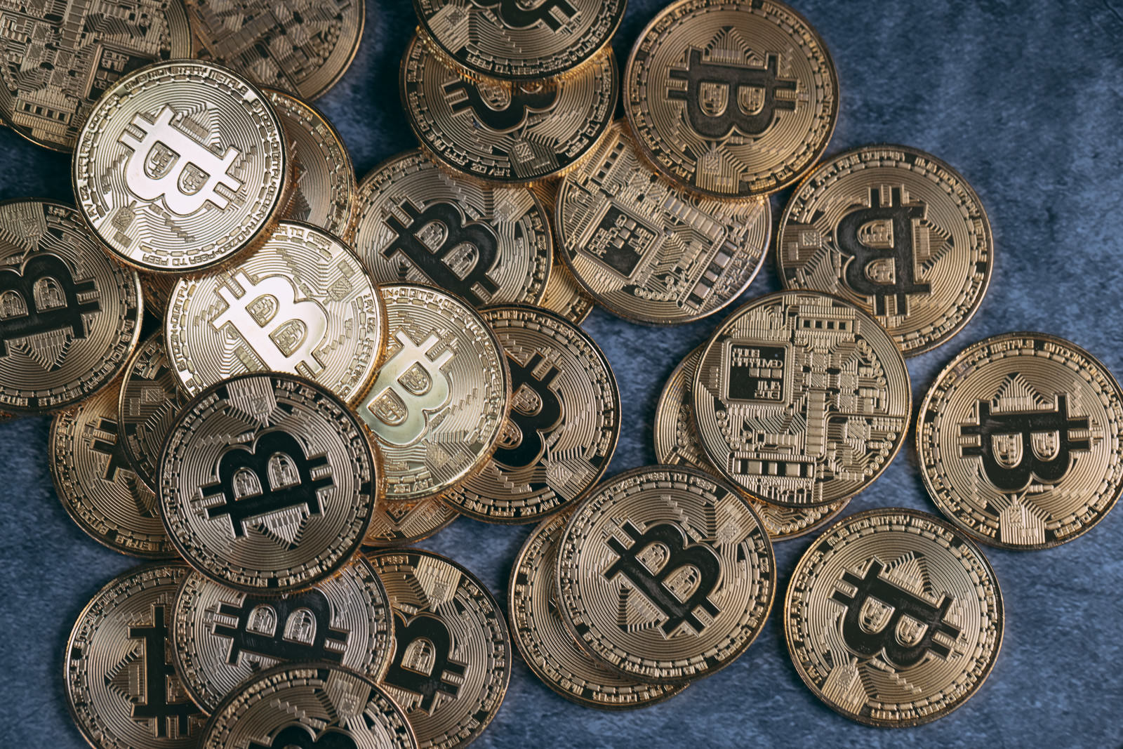 青い背景に散らばる金色のビットコインコイン複数枚