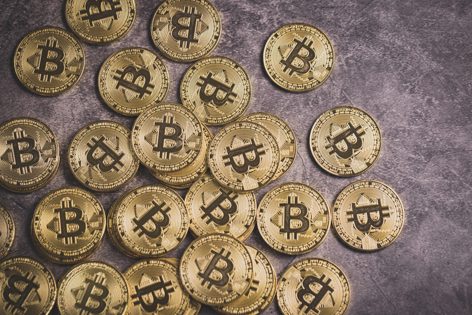 石のような背景に散らばって配置された金色のビットコインコイン