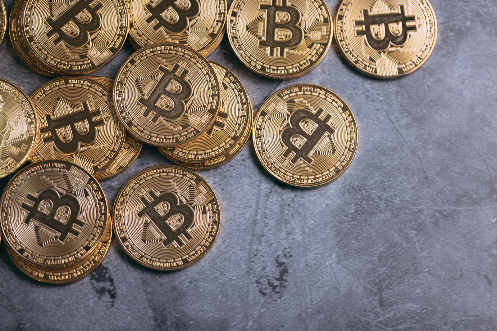 グレーの背景に散らばって置かれた複数のゴールドカラーのビットコイン