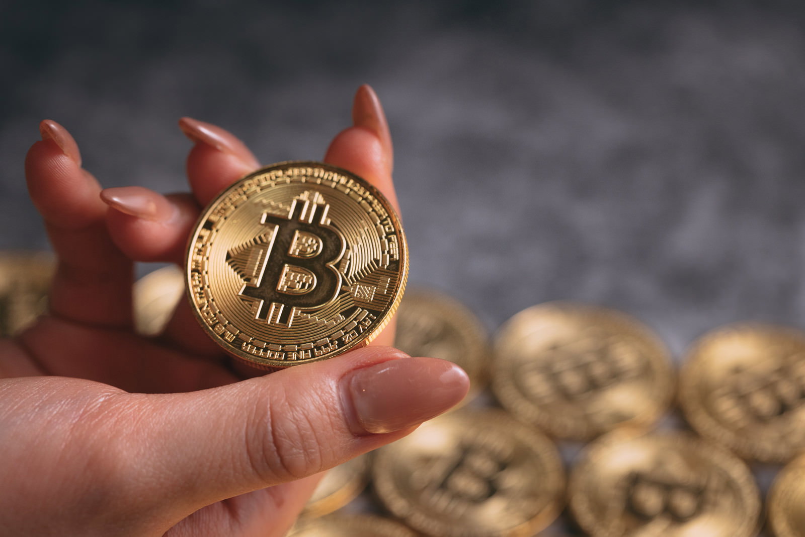 金色のビットコインを指先で掴む女性の右手