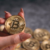 ビットコインを指先で掴む女性の右手とコインの写真