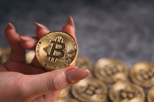 ビットコインを指先で掴む女性の右手とコイン