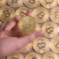 ビットコインを指でつまむ女性の右手の写真