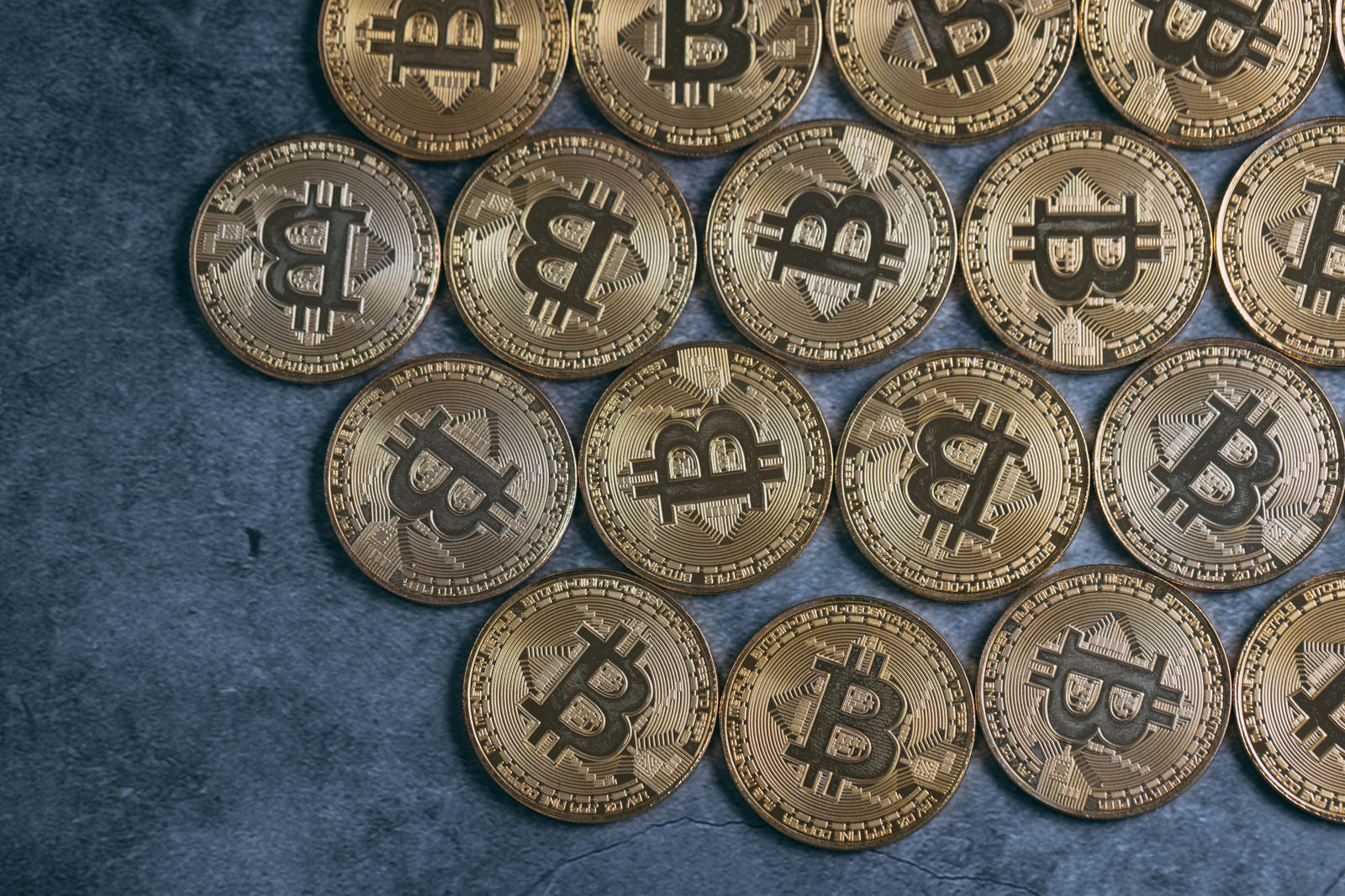青い背景に右寄せで並べられた金色のビットコインコイン