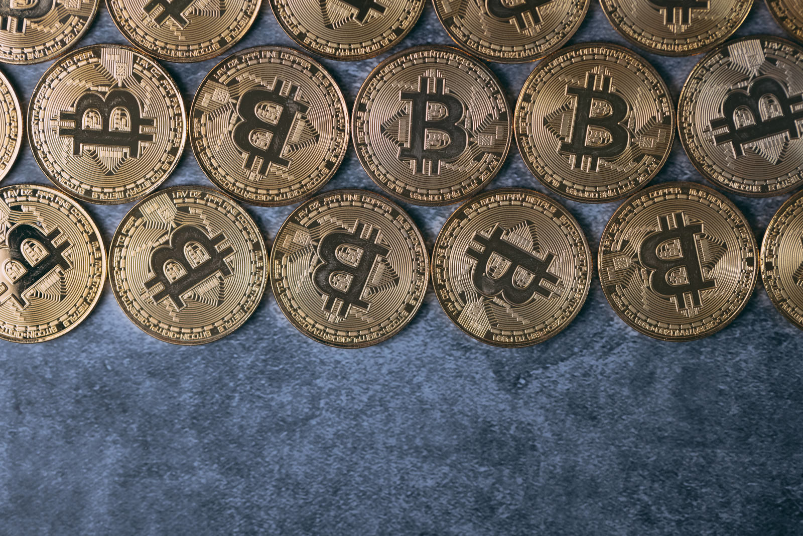 青い背景に金色のビットコインが規則正しく並べられた様子
