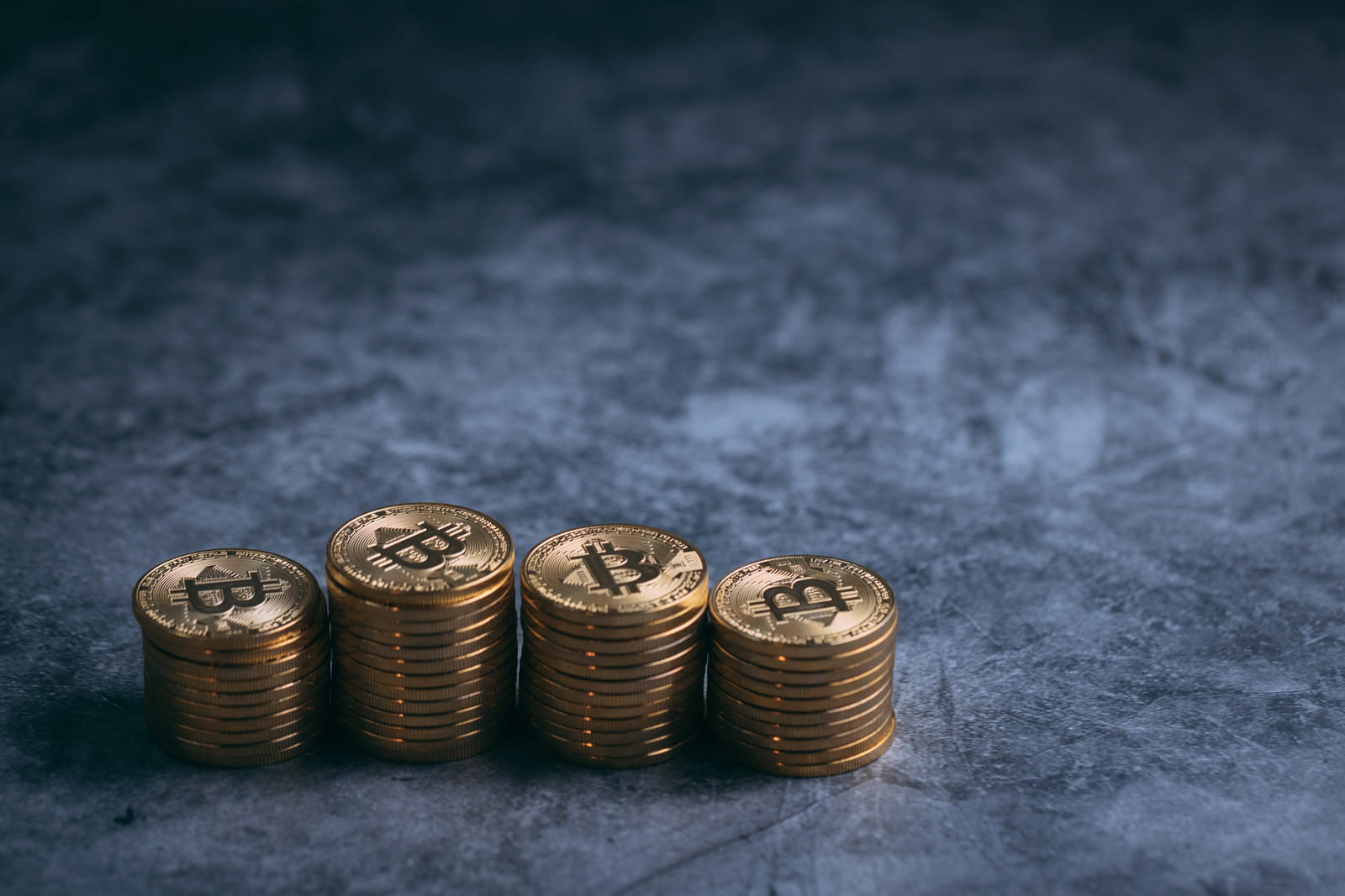 ビットコインのロゴが刻印された4枚の金貨が縦に積み重ねられている
