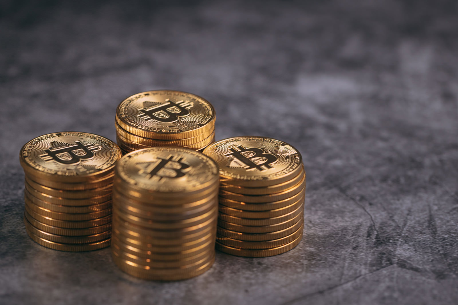 暗いグレーの背景に金色のビットコインが4つの山に積み重ねられている