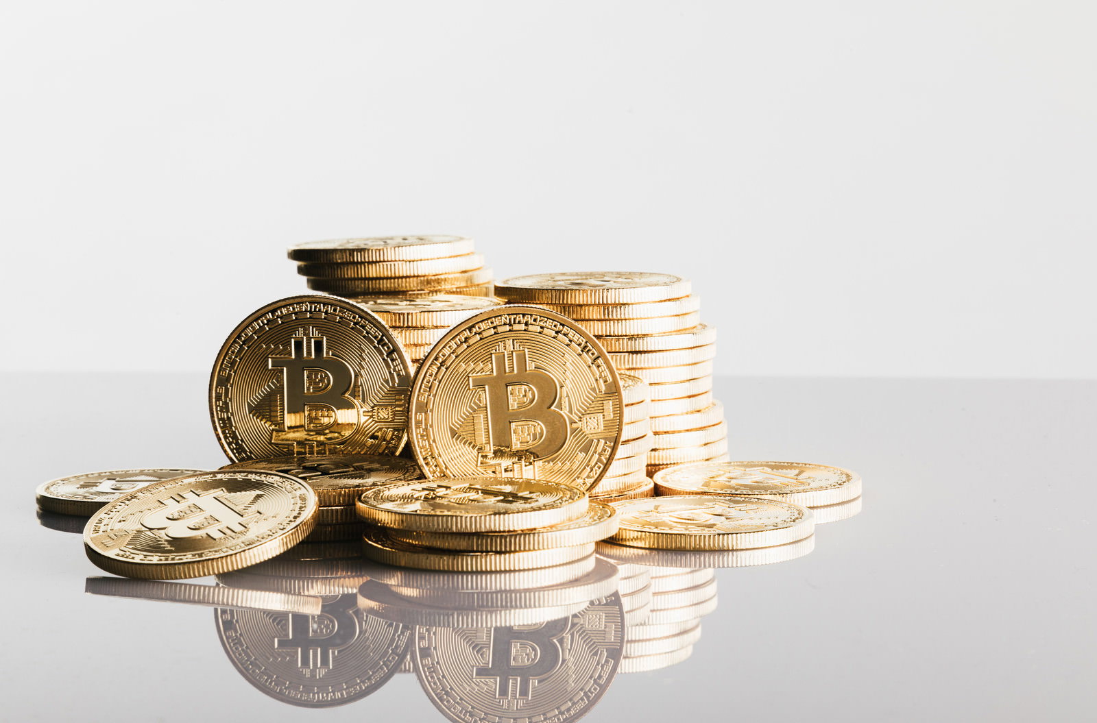 白い背景に積み重なったビットコインと金色のコインの反射