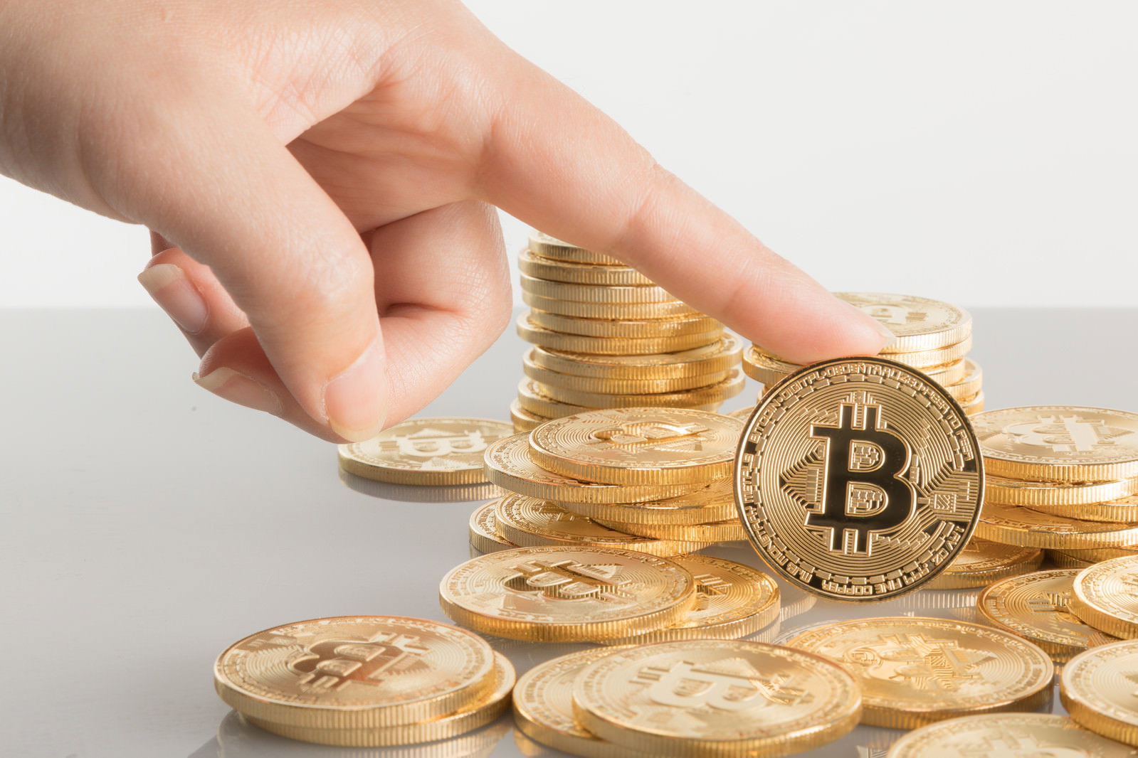 積み重ねられた金色のビットコインの上に手をかざしている様子