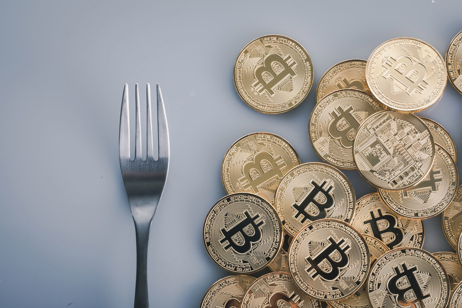 テーブル上に置かれたシルバーのフォークと金色のビットコイン