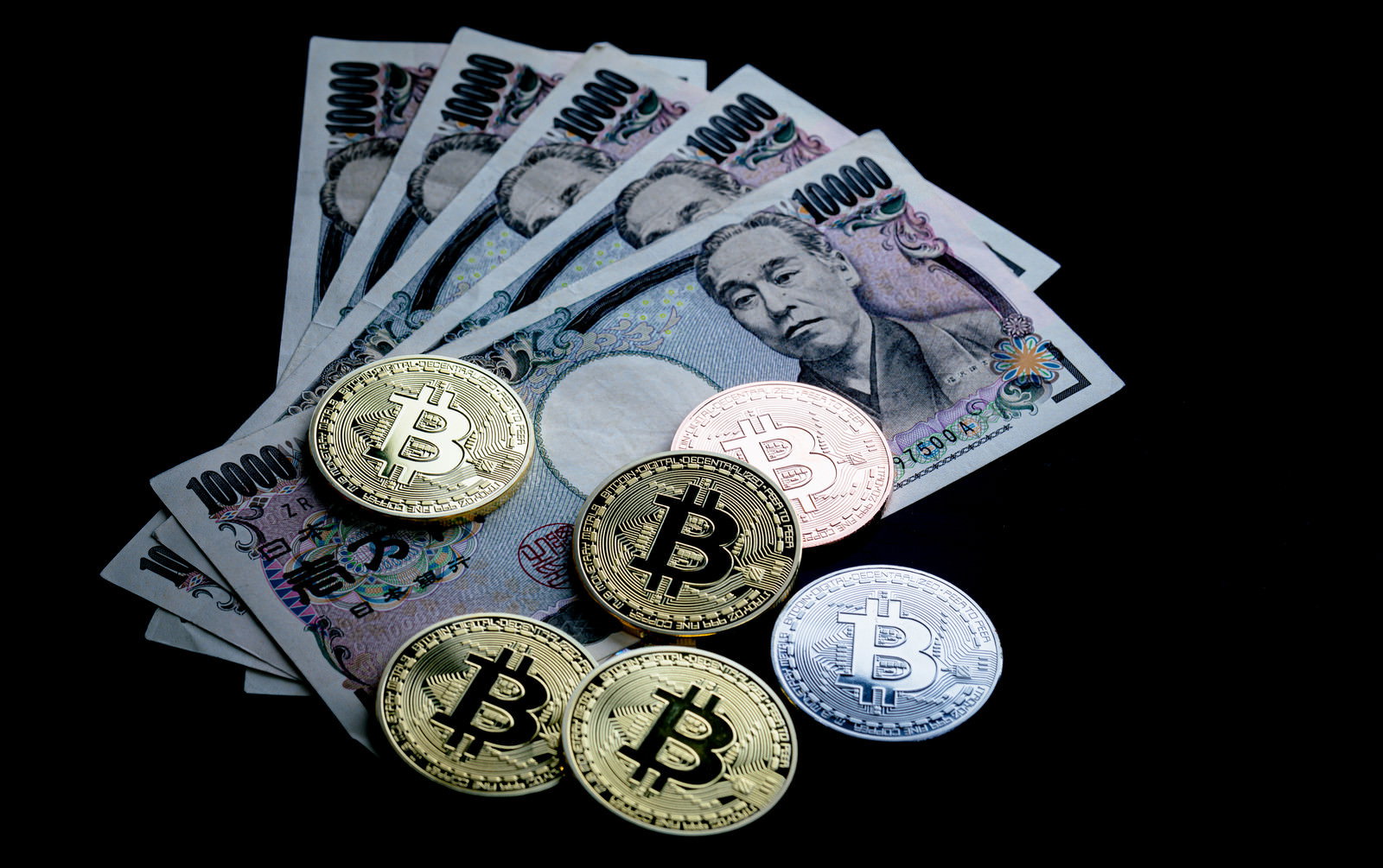 黒い背景に金色のビットコインコインと一万円札が並んで配置されている