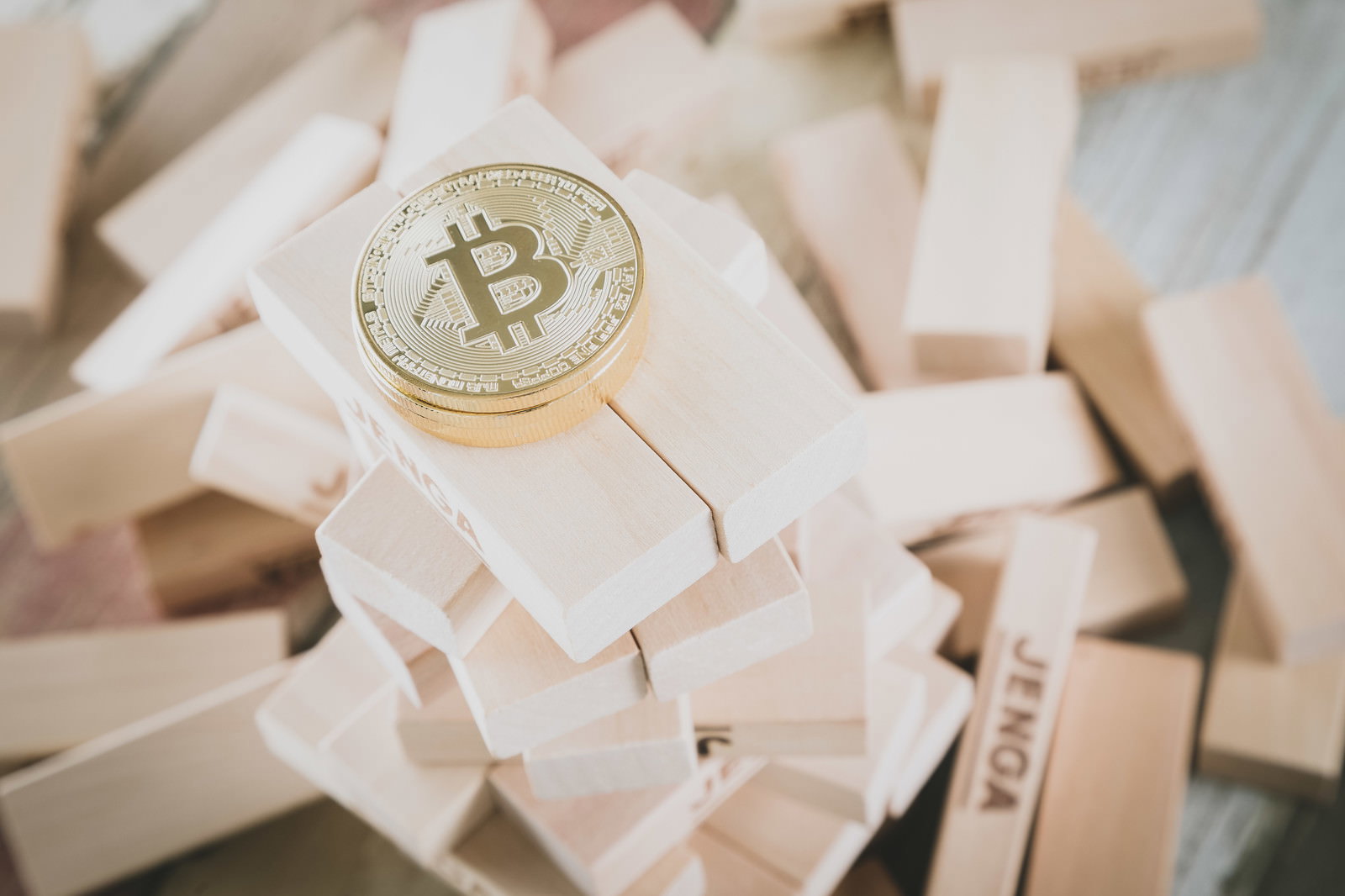 白いジェンガブロックの積み重ねた頂点に置かれた金色のビットコインコイン