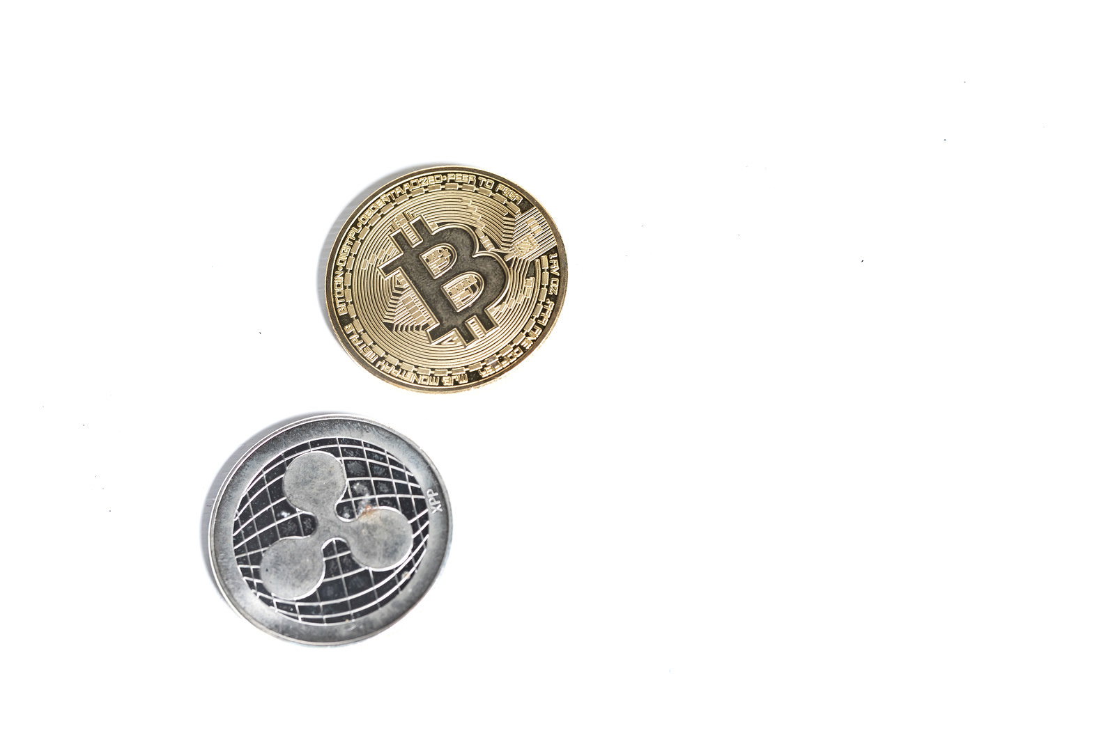 白い背景に金色のビットコインと銀色のリップルのコインが並んでいる