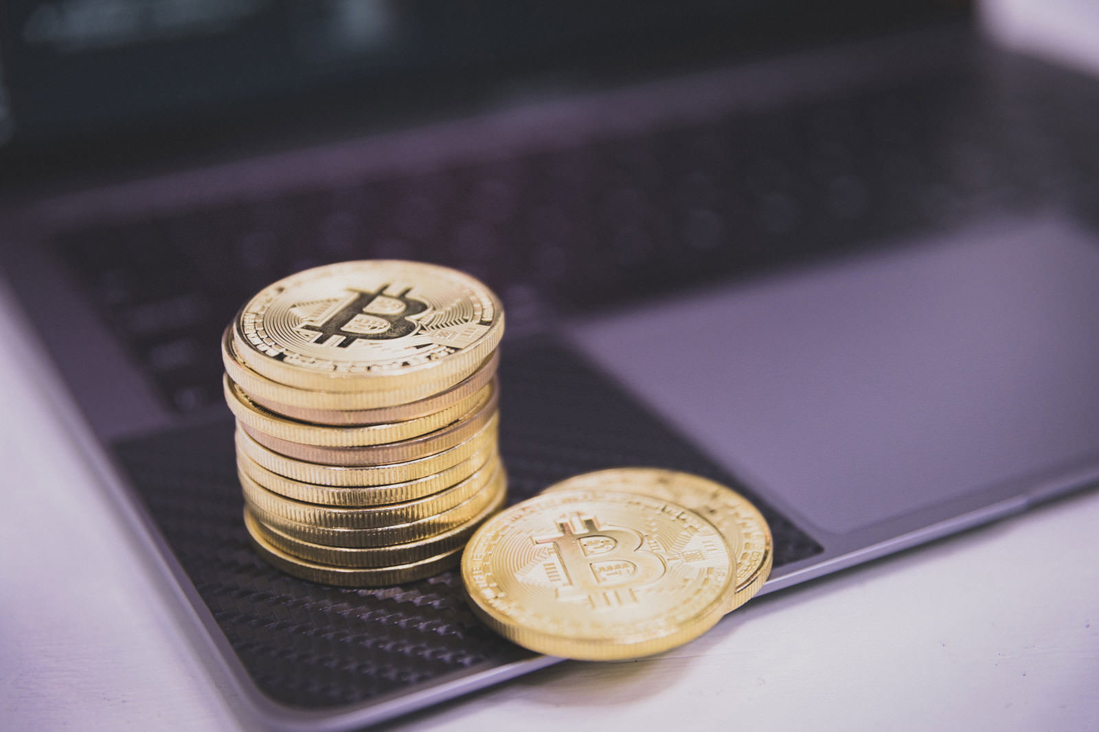 ノートパソコンのキーボードの上に積み重ねられた金色のビットコイン