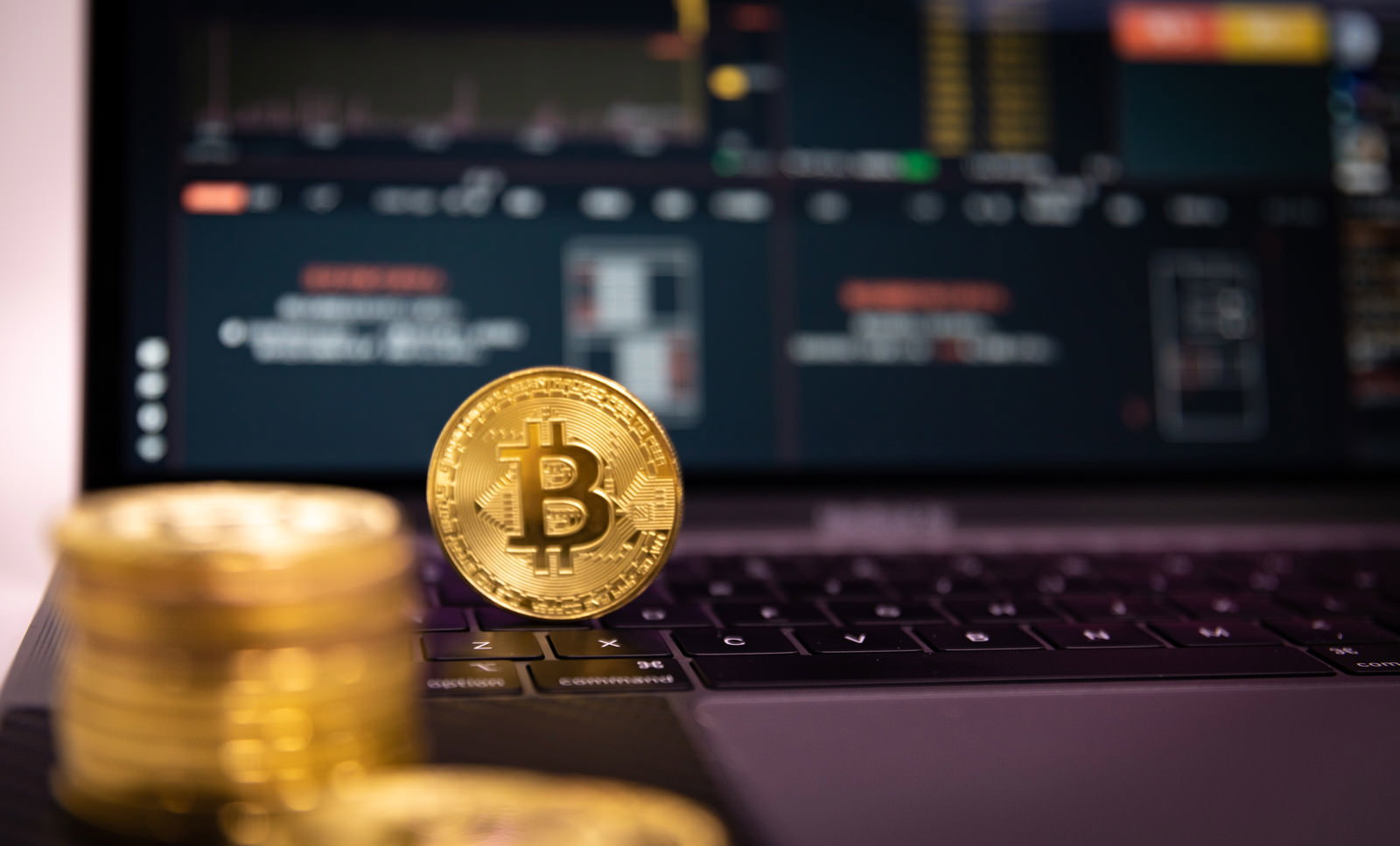 ノートパソコンのキーボード上に置かれた金色のビットコインと取引画面