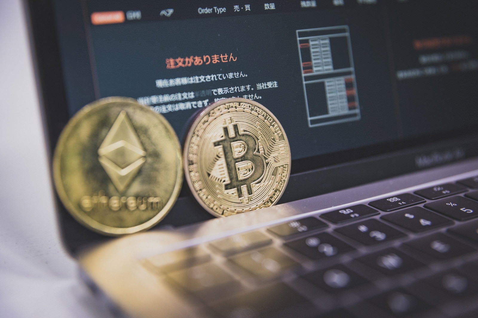ノートパソコンのキーボード上に置かれたビットコインとイーサリアムのコイン