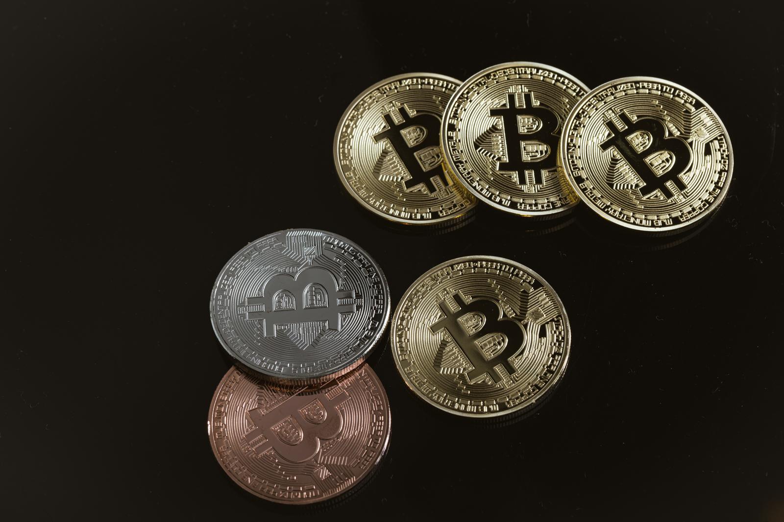 黒い背景に複数のビットコインコイン。金色、銀色、銅色の異なる3種類のコイン
