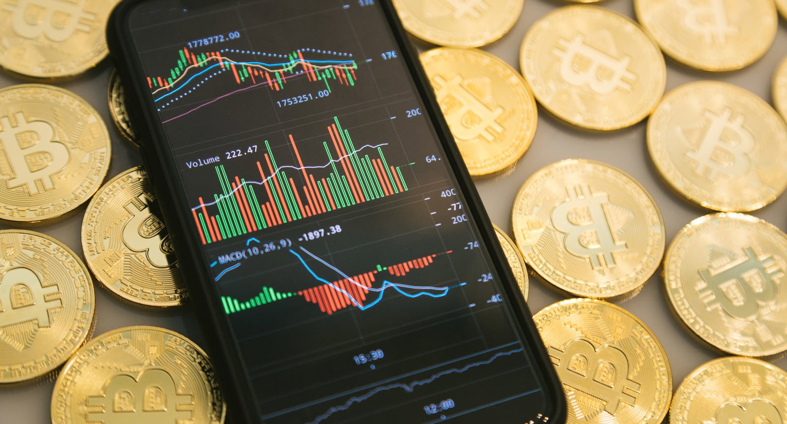 ビットコインの金貨に囲まれ、価格チャートが表示されたスマートフォン