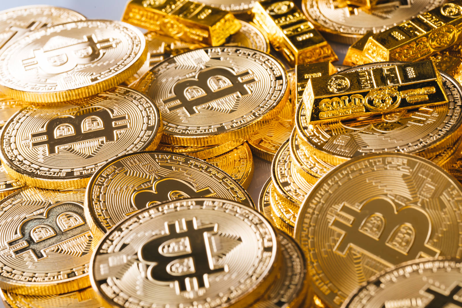 Bマークが刻印された金色のビットコインと金塊が積み重なる様子