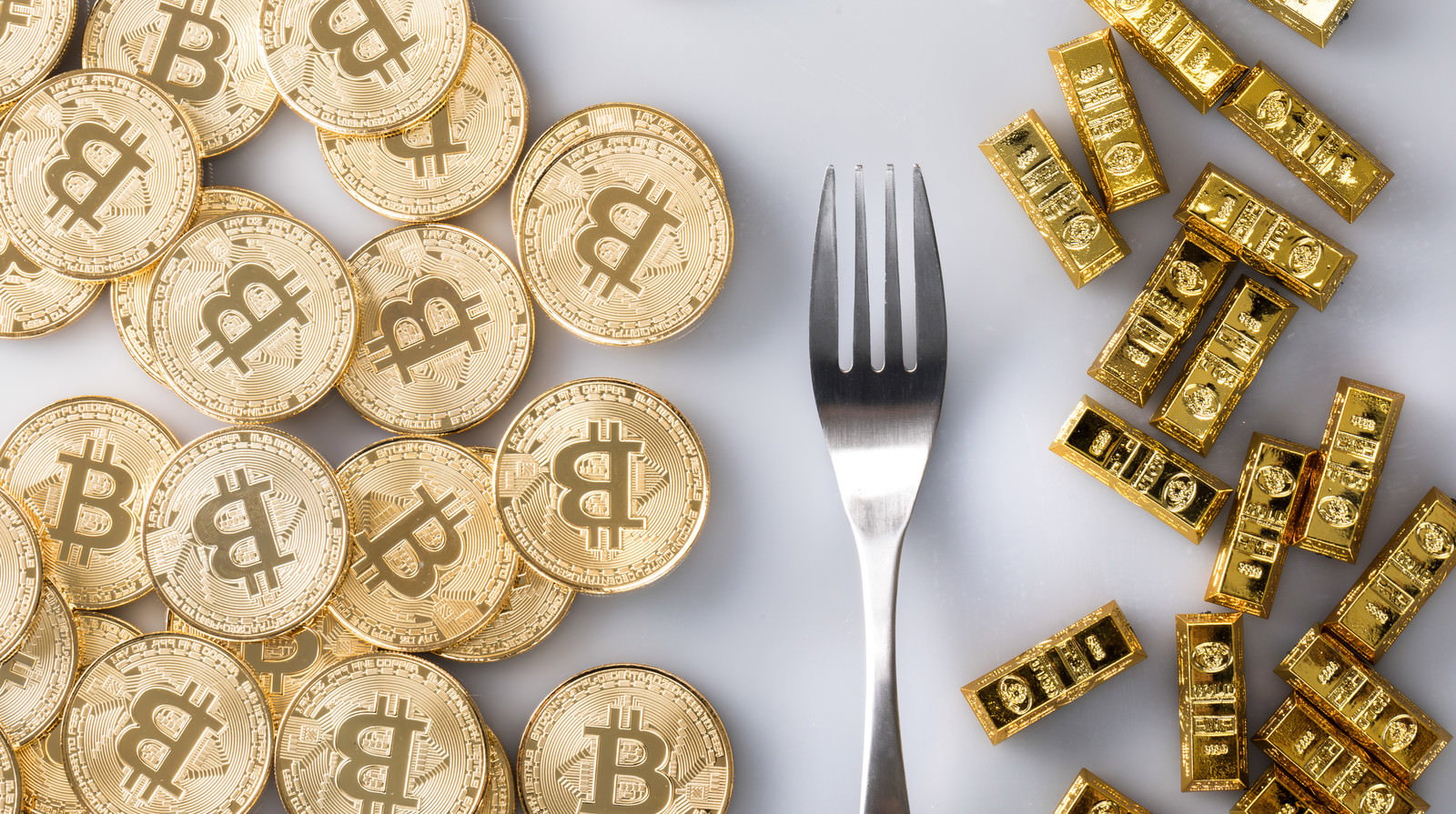 ビットコイン金貨とゴールドインゴット、フォークが配置された白背景の写真
