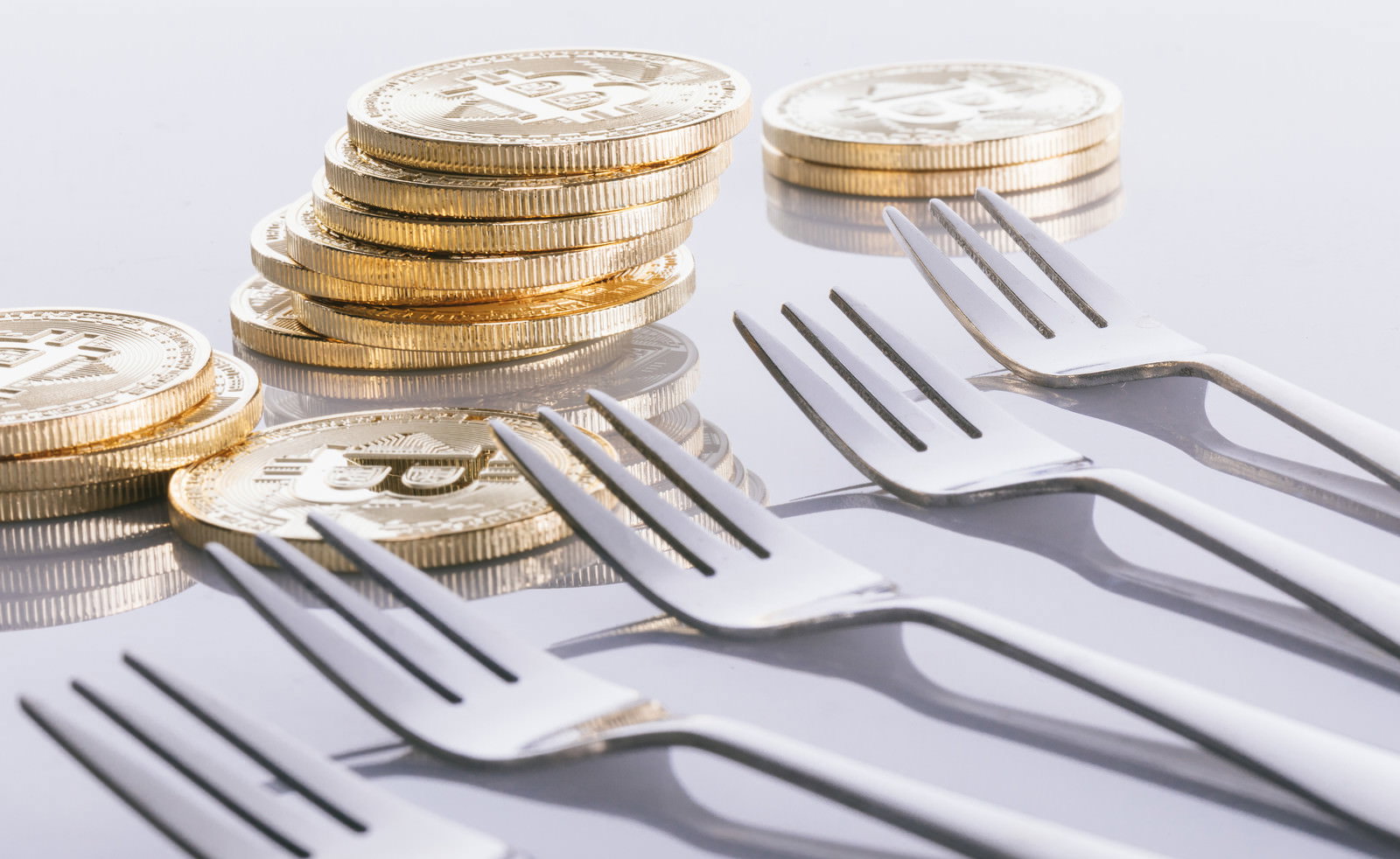 白い背景に並んだ複数のフォークと金色のビットコイン風コイン