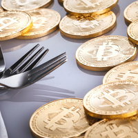 ビットコインとハードフォークを表現した金貨とフォークの静物の写真