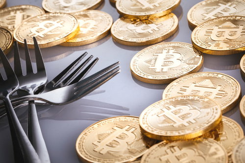 ビットコインとハードフォークを表現した金貨とフォークの静物