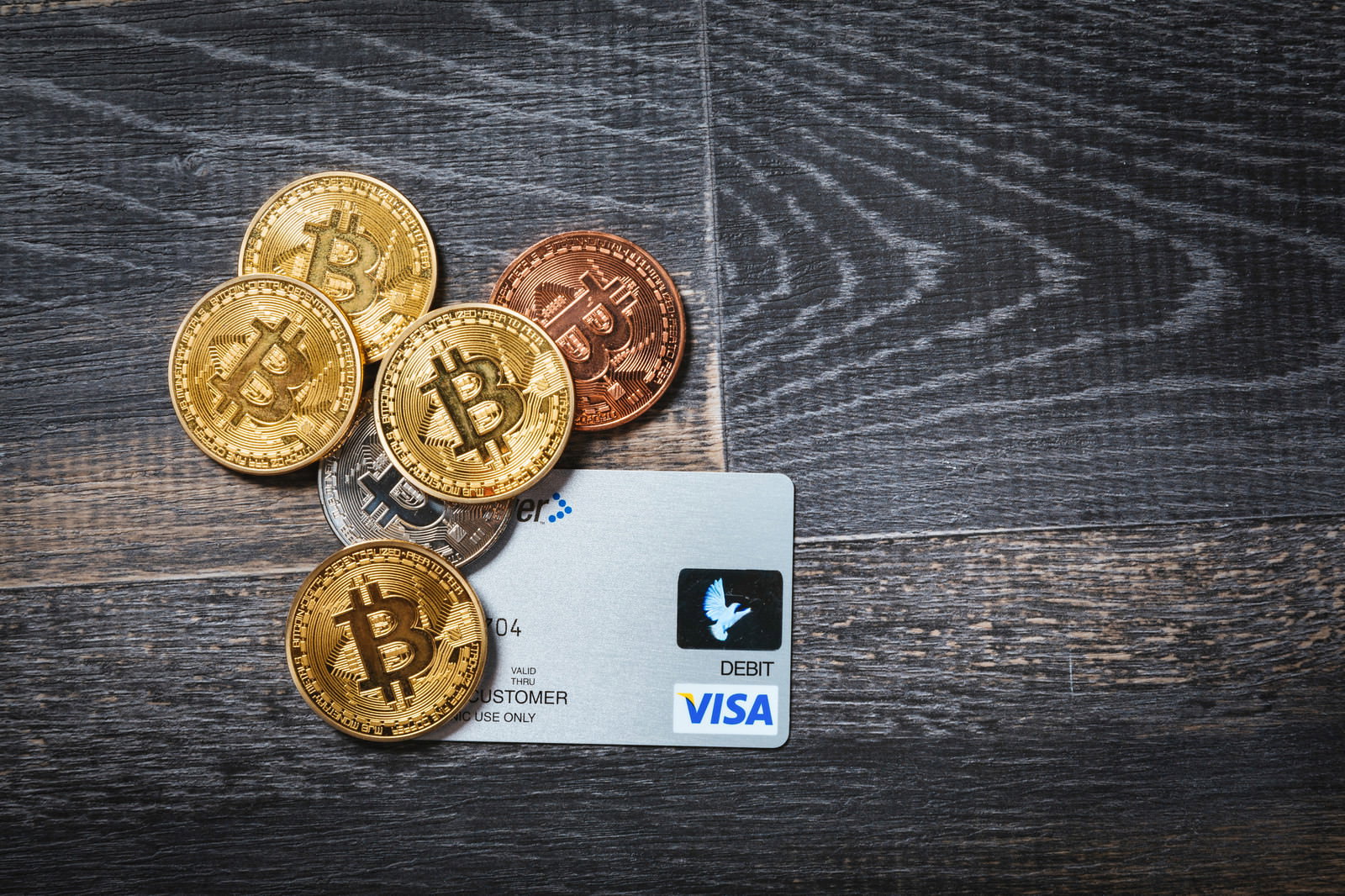 木目調の背景に金色のビットコインとVISAデビットカードが配置された様子