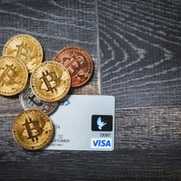 金色のビットコインとVISAデビットカードが並ぶ仮想通貨と決済手段の写真