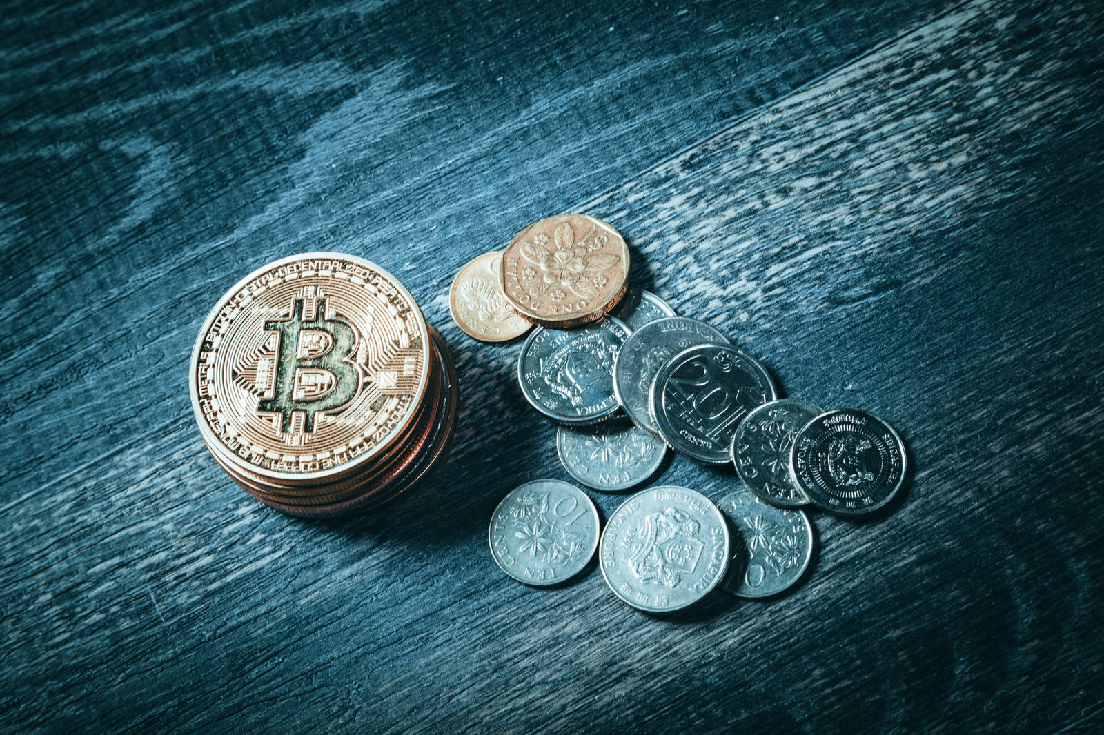 木目調の背景に置かれた金色のビットコインと銀色のシンガポールドルコイン
