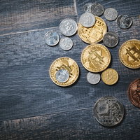 木製テーブルに散らばったビットコインと各国硬貨の写真