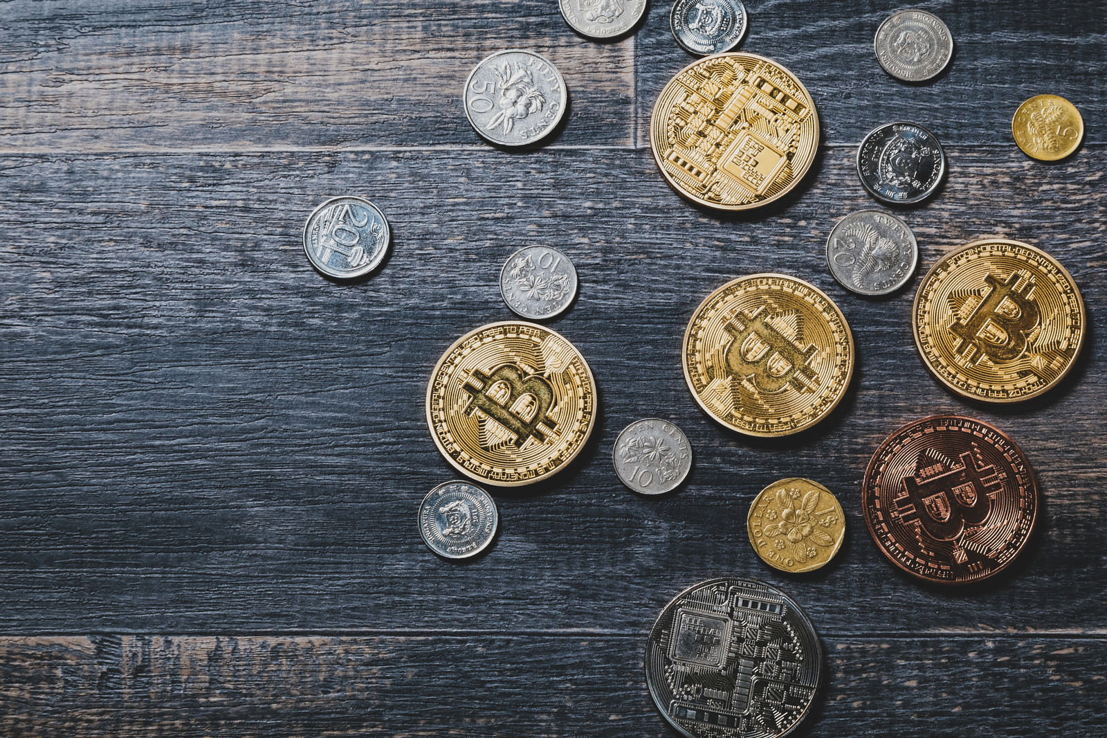 木製テーブルに散らばるビットコインとシンガポールドルのコイン