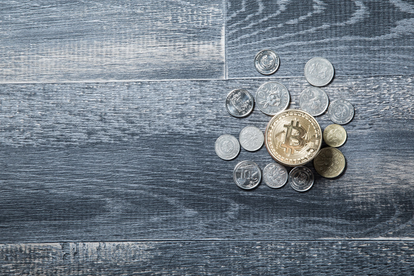 木目調の背景に金色のビットコインと各国の硬貨が散らばっている