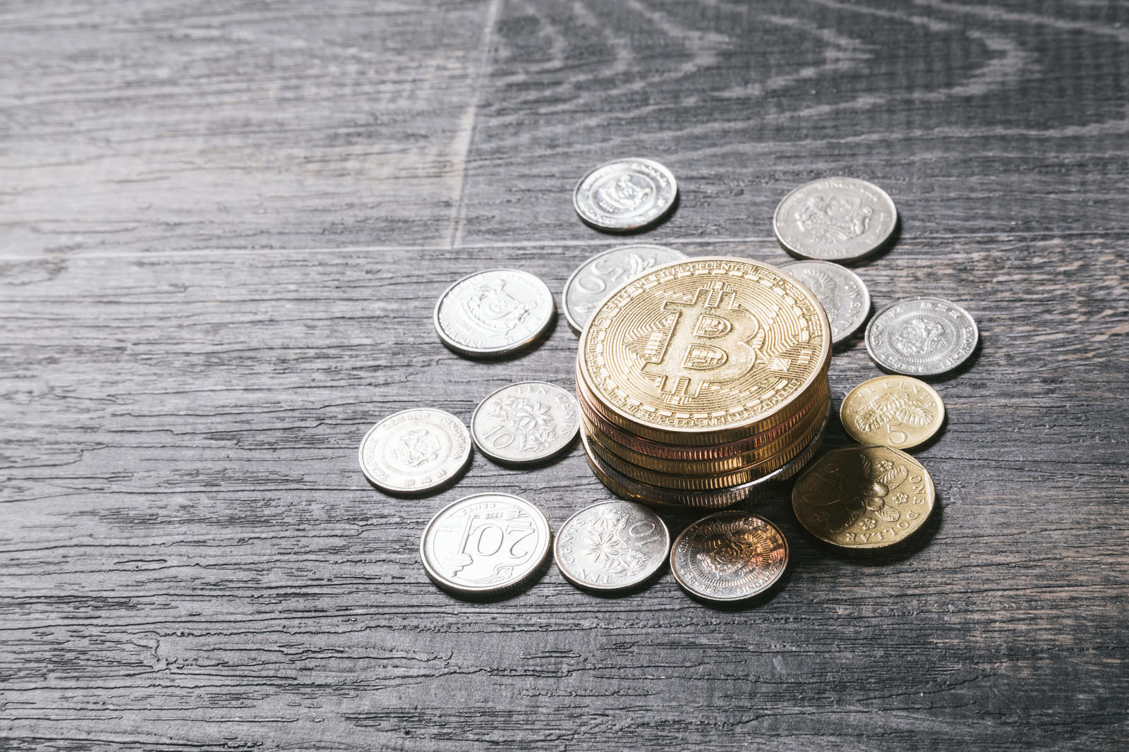 木製テーブル上に散らばるシンガポールドル硬貨と中央の金色ビットコイン