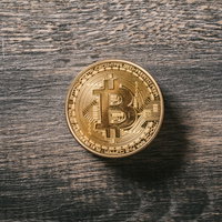 木目のテーブルに置かれたビットコインの金貨の写真