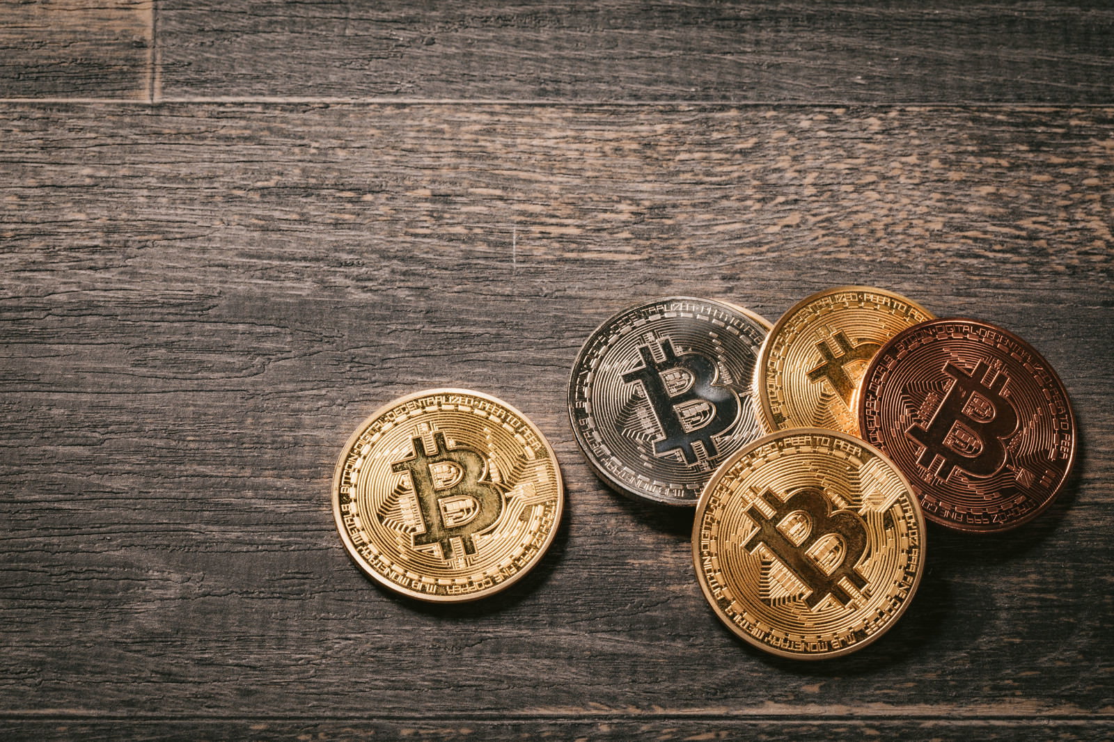 木目調の背景に金色のビットコインコインが複数枚置かれている