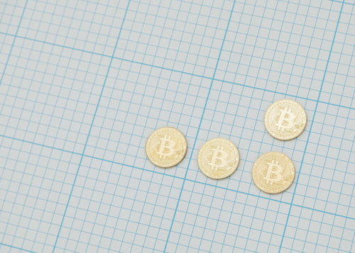 方眼紙の上に置かれた金色のビットコイン硬貨の投資
