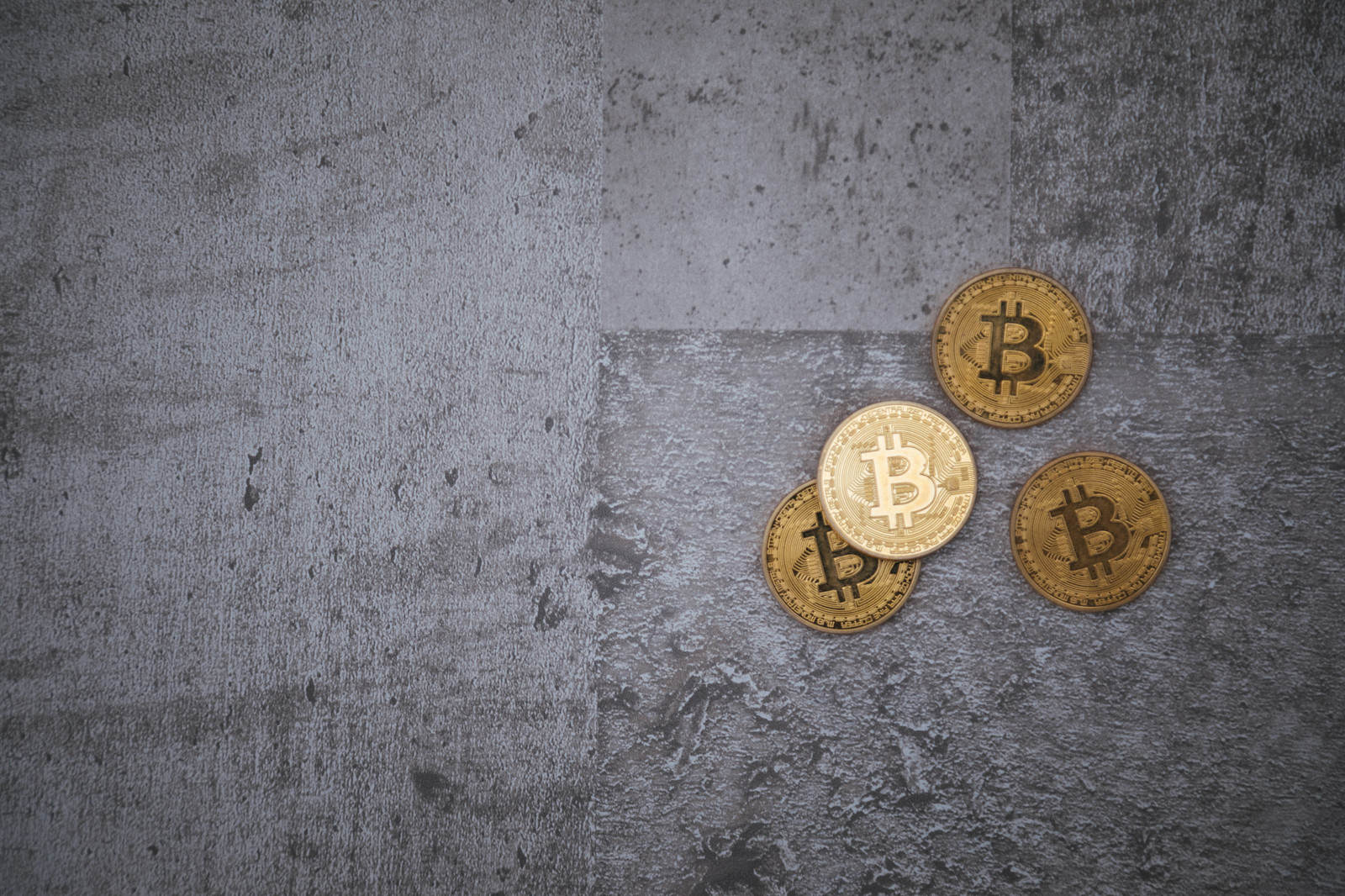 灰色のコンクリート床に置かれた3枚の金色のビットコイン硬貨