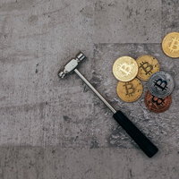 コンクリート床に散らばるビットコインとハンマーの写真