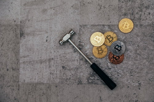 コンクリート床に散らばるビットコインとハンマー