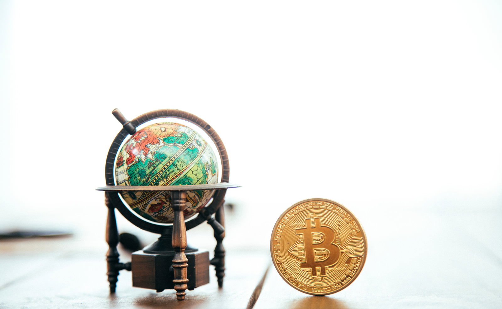 木製スタンドの地球儀と金色のビットコインが並んで配置された写真