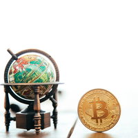 木製スタンドの地球儀と金色のビットコインの写真