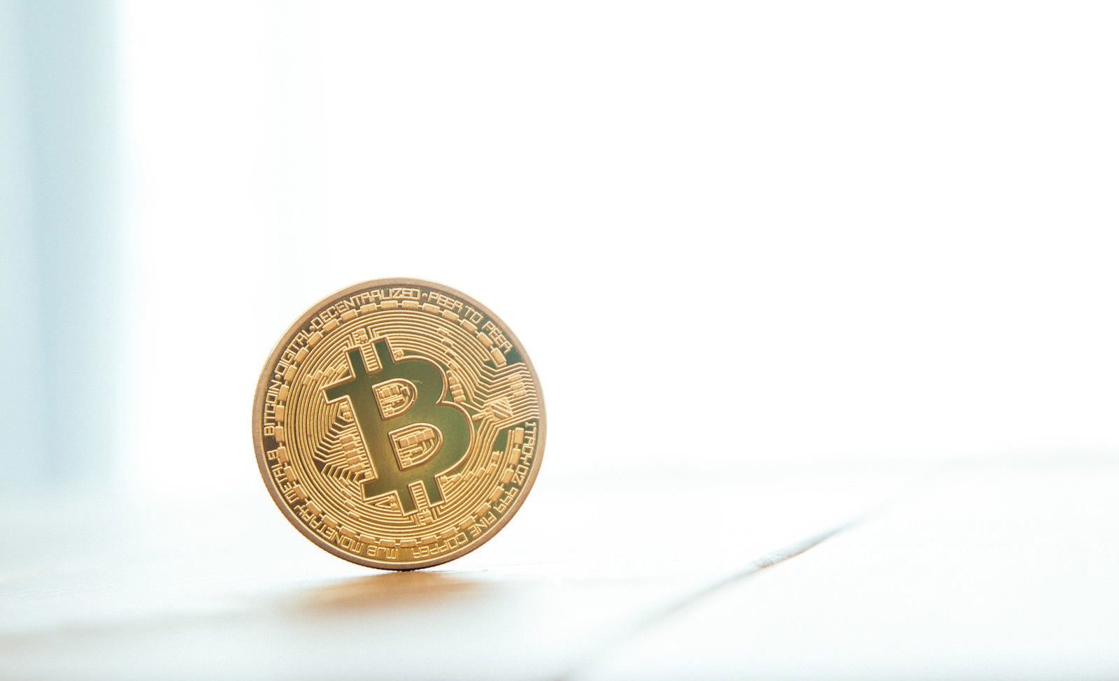 白い台の上に斜めに立てられた金色のビットコイン模型コイン