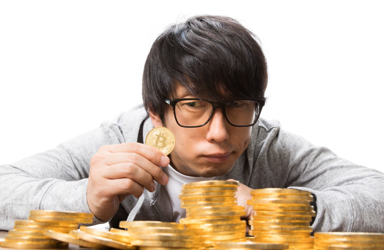 ビットコイン硬貨を持つ眼鏡をかけた男性と積み重なった金貨［モデル：大川竜弥］