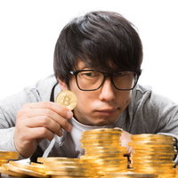 ビットコイン硬貨を手に取り眺める男性投資家の写真