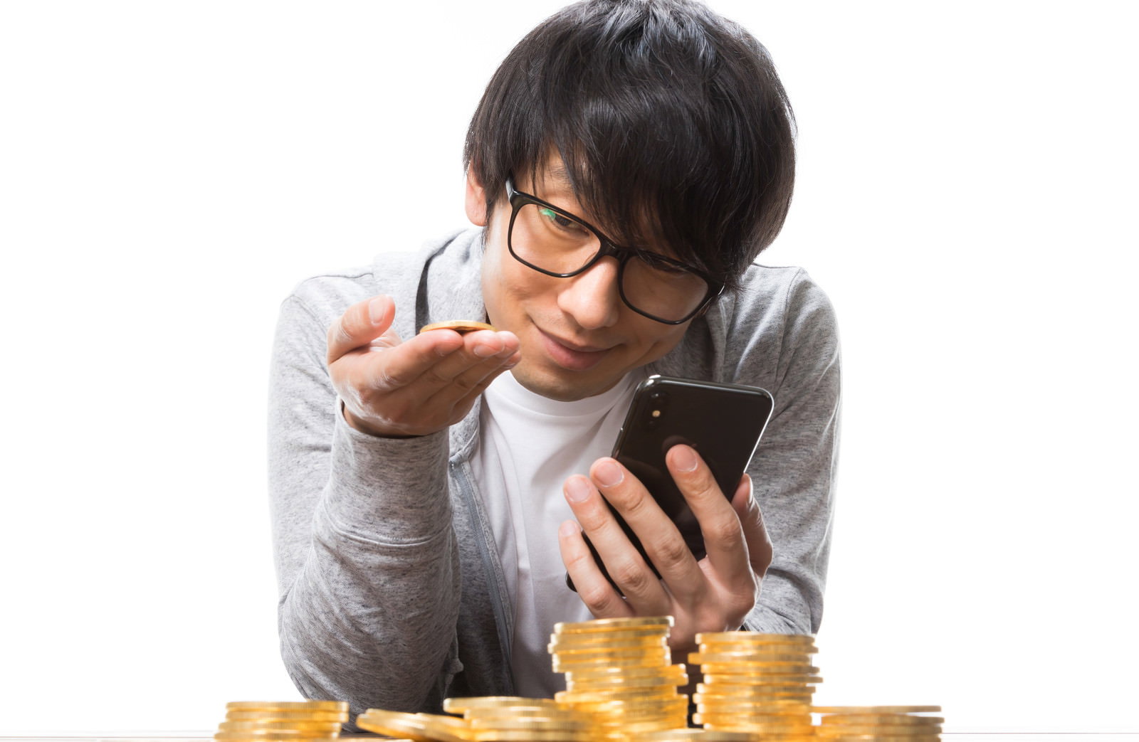 スマートフォンを持つ男性が金貨に触れている［モデル：大川竜弥］