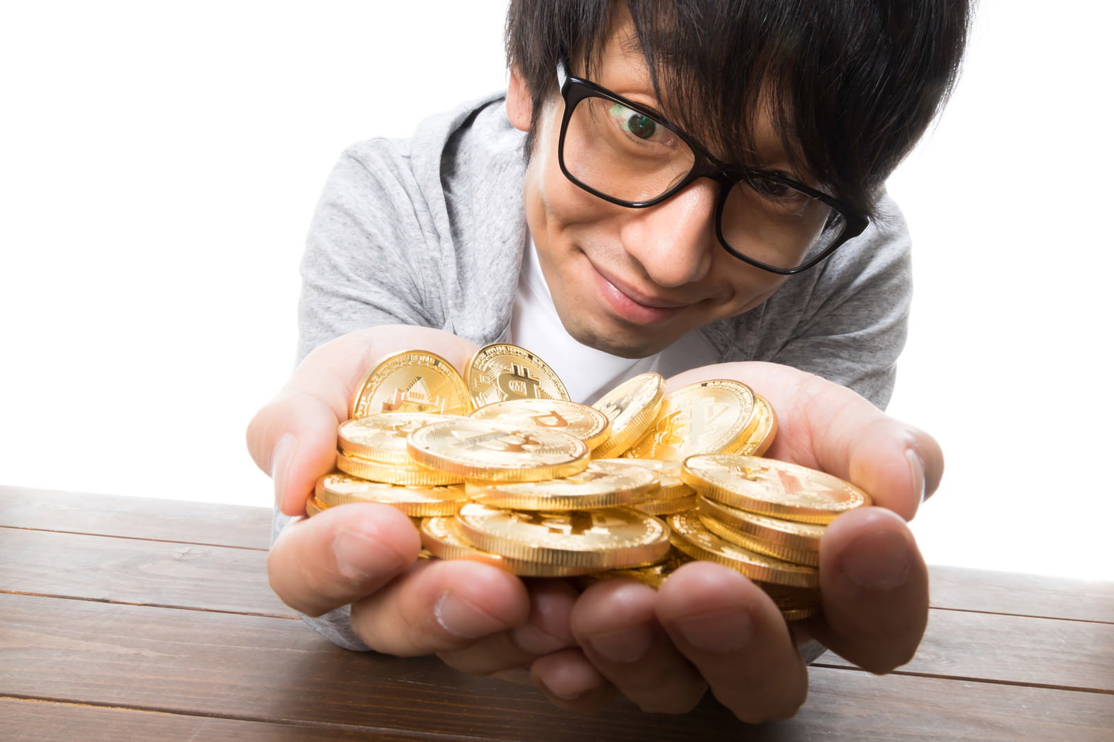 眼鏡をかけた男性が積み重ねた金貨を両手に広げて持ち笑顔で見つめている［モデル：大川竜弥］