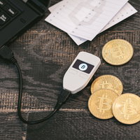 仮想通貨を保管するハードウェアウォレットTREZORと金色のビットコインの写真