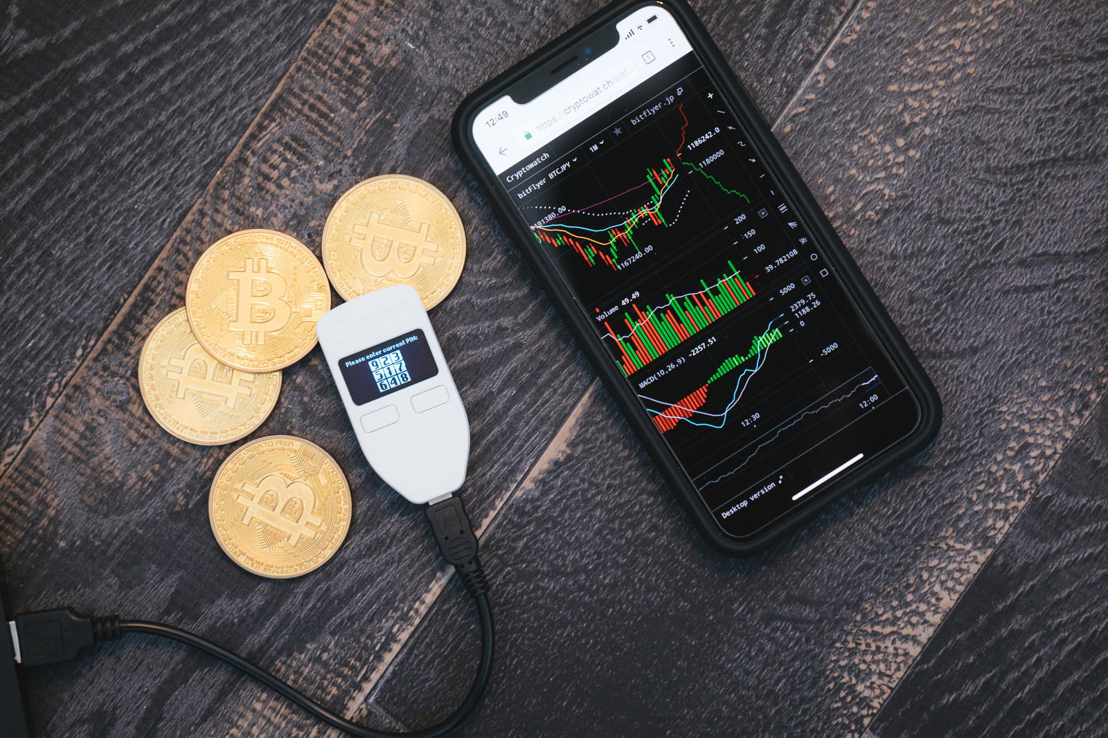 木製テーブル上のスマートフォンのビットコインチャートとTREZORハードウェアウォレット