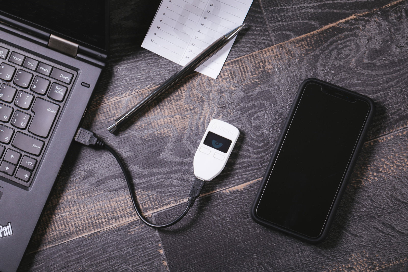ノートパソコンに接続されたTREZORハードウェアウォレットとスマートフォンが机上に配置された様子